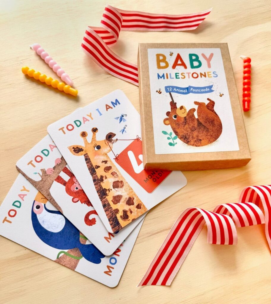 Baby milestone cards with animal illustrations and a matching gift box on wood.