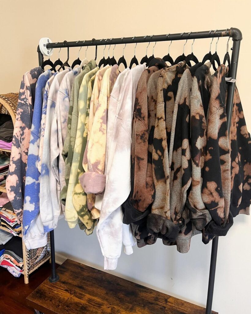 Tie-dye sweatshirts in multiple colors hanging on a black metal clothing rack.