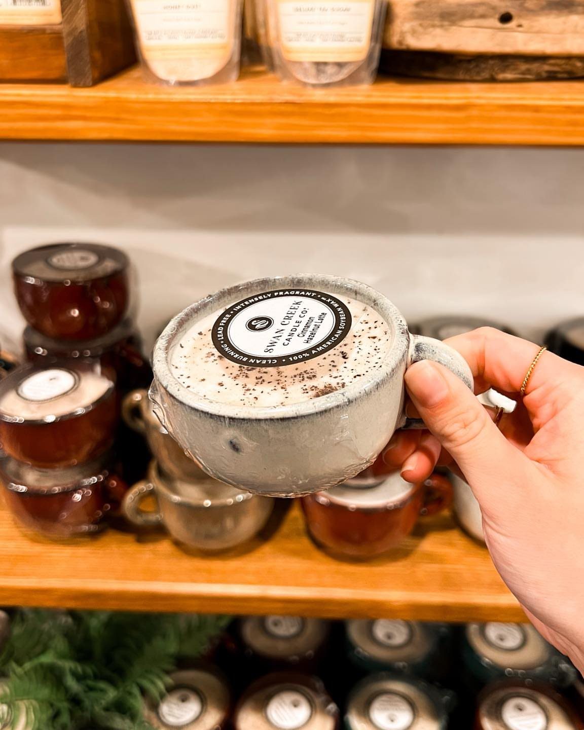 Hand holding a candle shaped like a grey coffee mug with cream wax.
