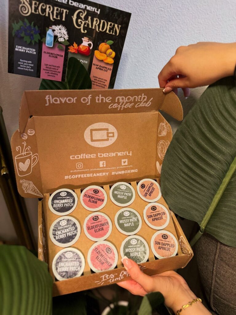 Open cardboard coffee subscription box containing twelve colorful coffee pods held by hands.