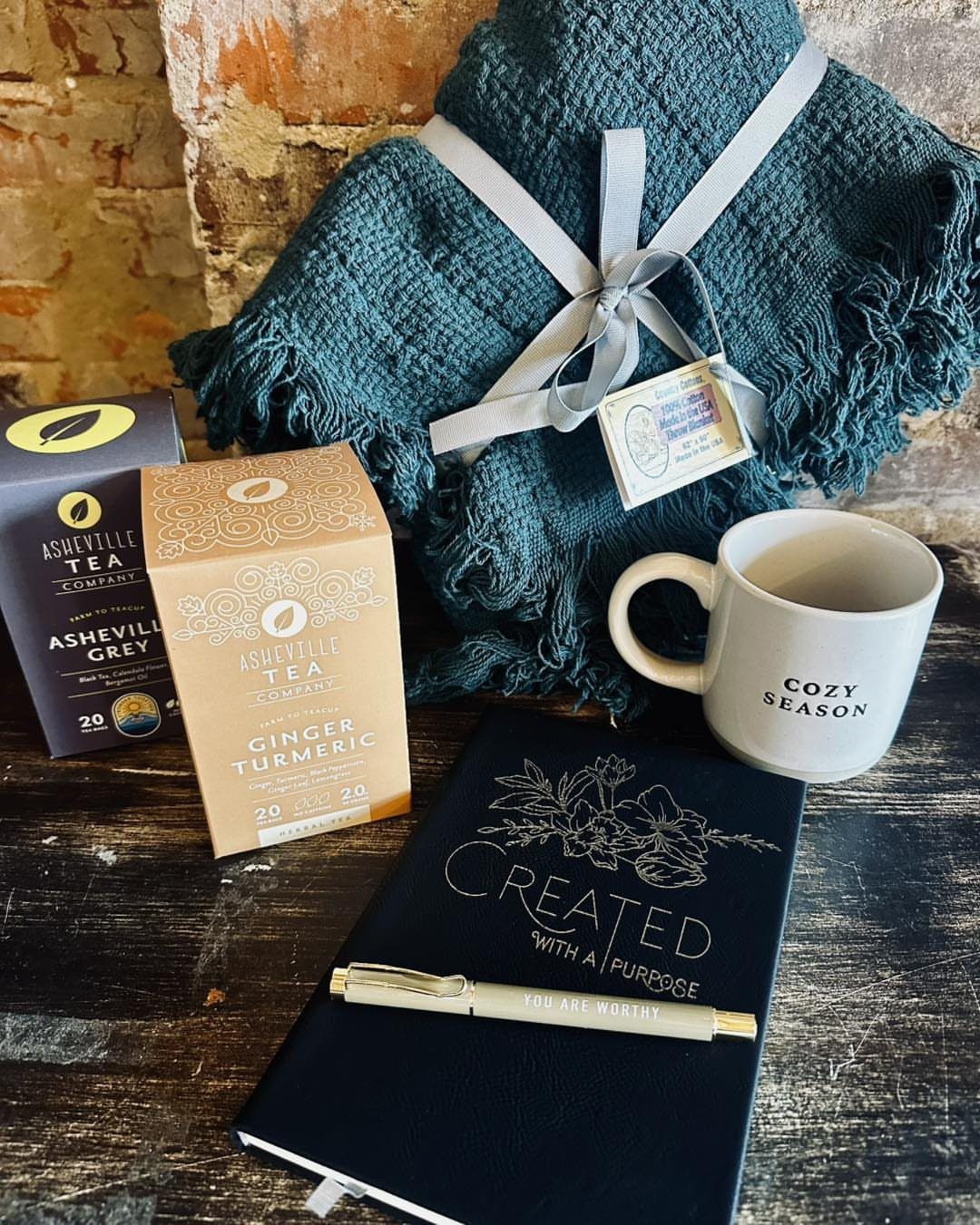 Teal blanket, tea boxes, a cozy season mug, and a notebook on wood.