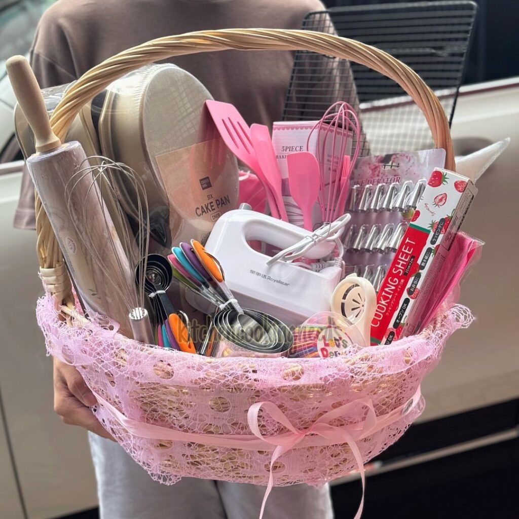 Wicker gift basket filled with pink baking tools and a white hand mixer.