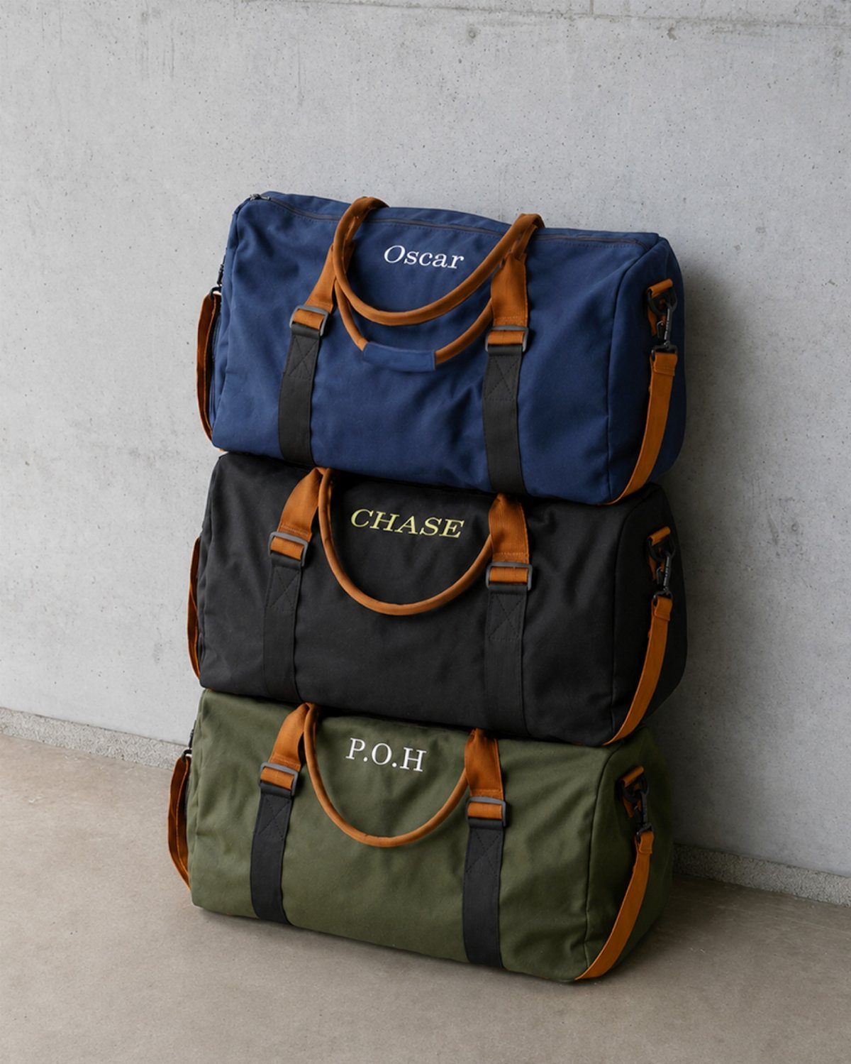 Three personalized canvas travel duffle bags in blue, black, and green stacked vertically.