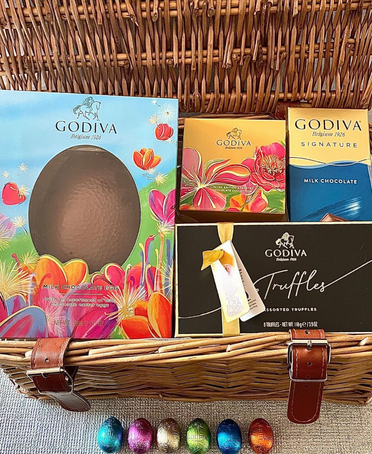 Woven wicker basket filled with Godiva chocolates and colorful metallic Easter eggs.