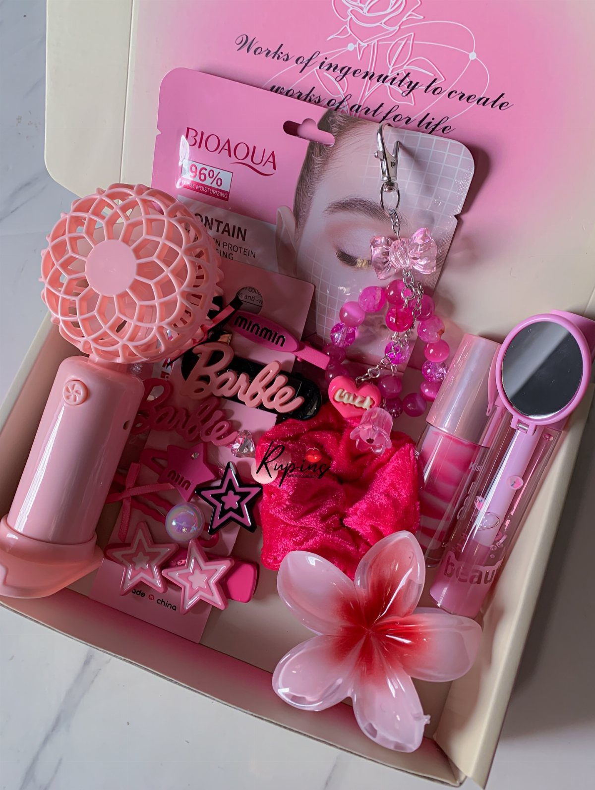 Pink beauty gift box containing a handheld fan, mirror, lip gloss, and accessories.