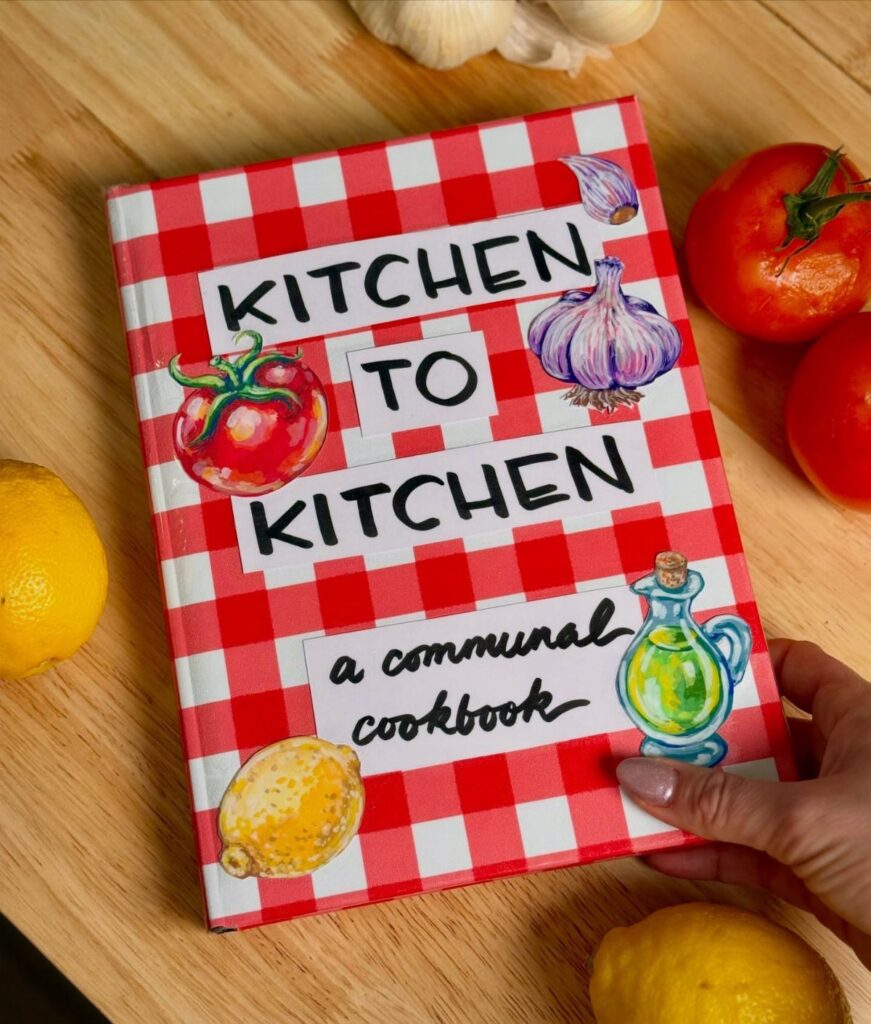 Communal cookbook with red checkered cover surrounded by fresh vegetables on wooden table