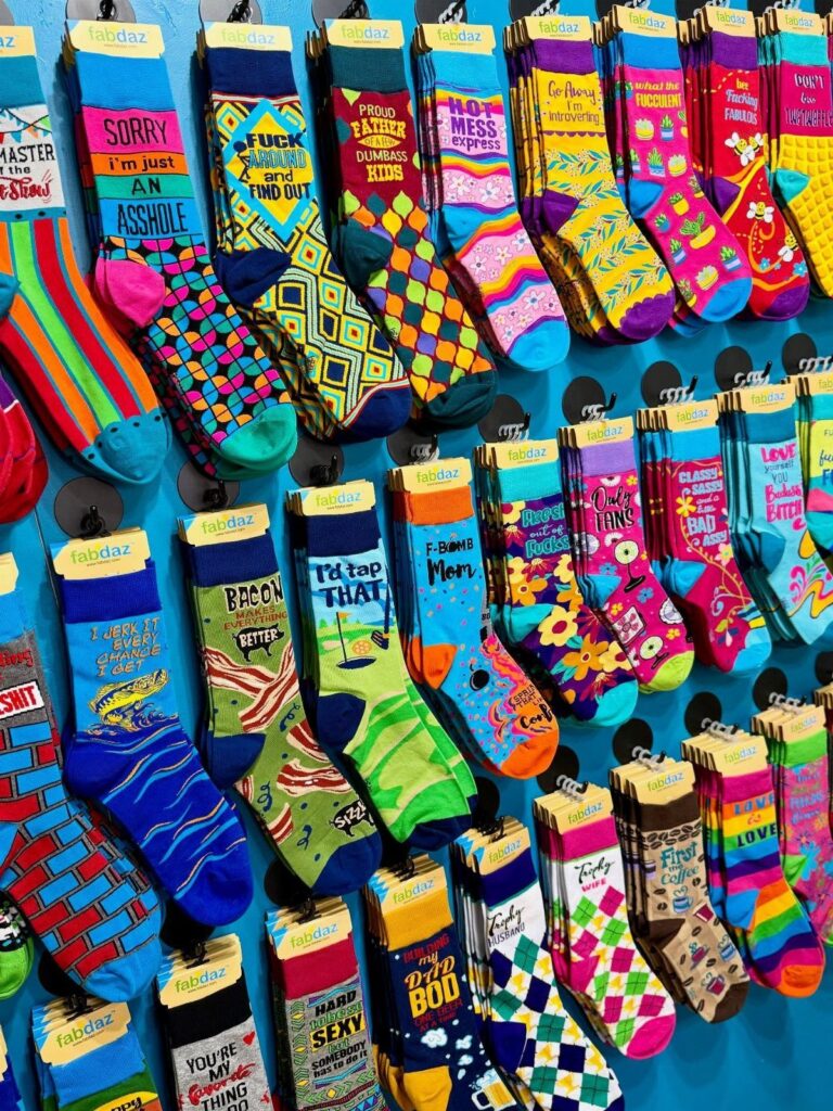 Colorful socks with funny prints and patterns hanging on a blue display wall.