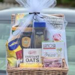 Wicker gift basket filled with food items wrapped in clear cellophane and tulle.