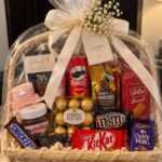 Wicker gift basket filled with assorted chocolates and snacks wrapped in clear cellophane.