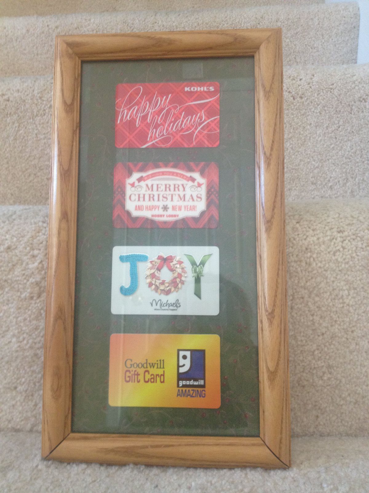 Four holiday-themed gift cards displayed vertically inside a light wooden picture frame.