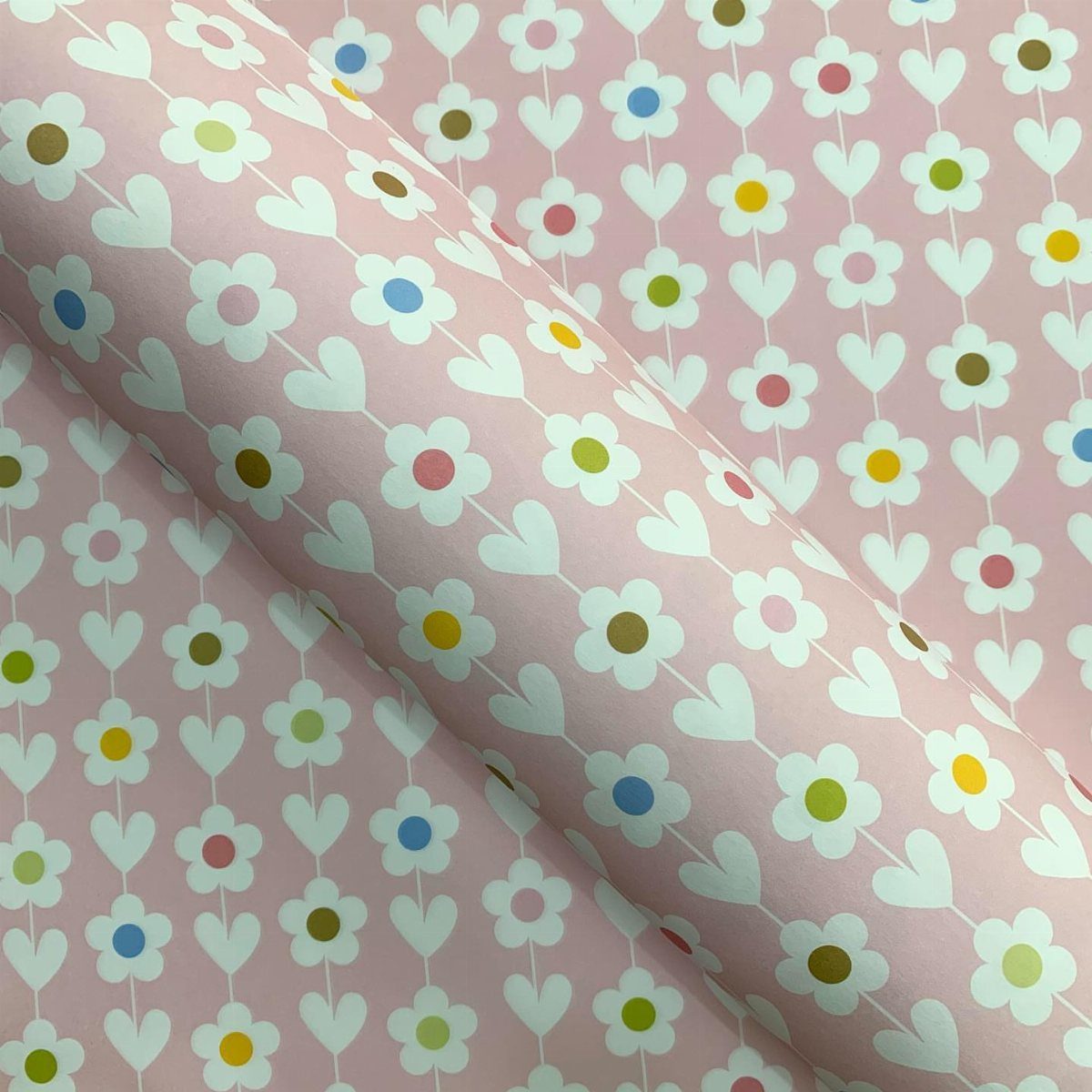 Pink wrapping paper roll with a white flower and heart pattern.