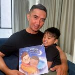Father and son sitting on a sofa holding a personalized children's book.