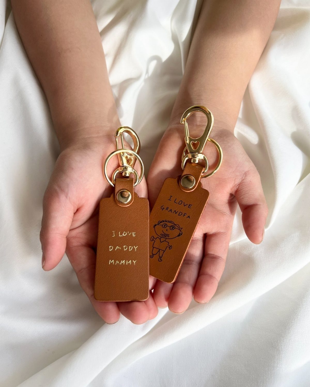 Two brown leather personalized keychains held in a child's open palms.
