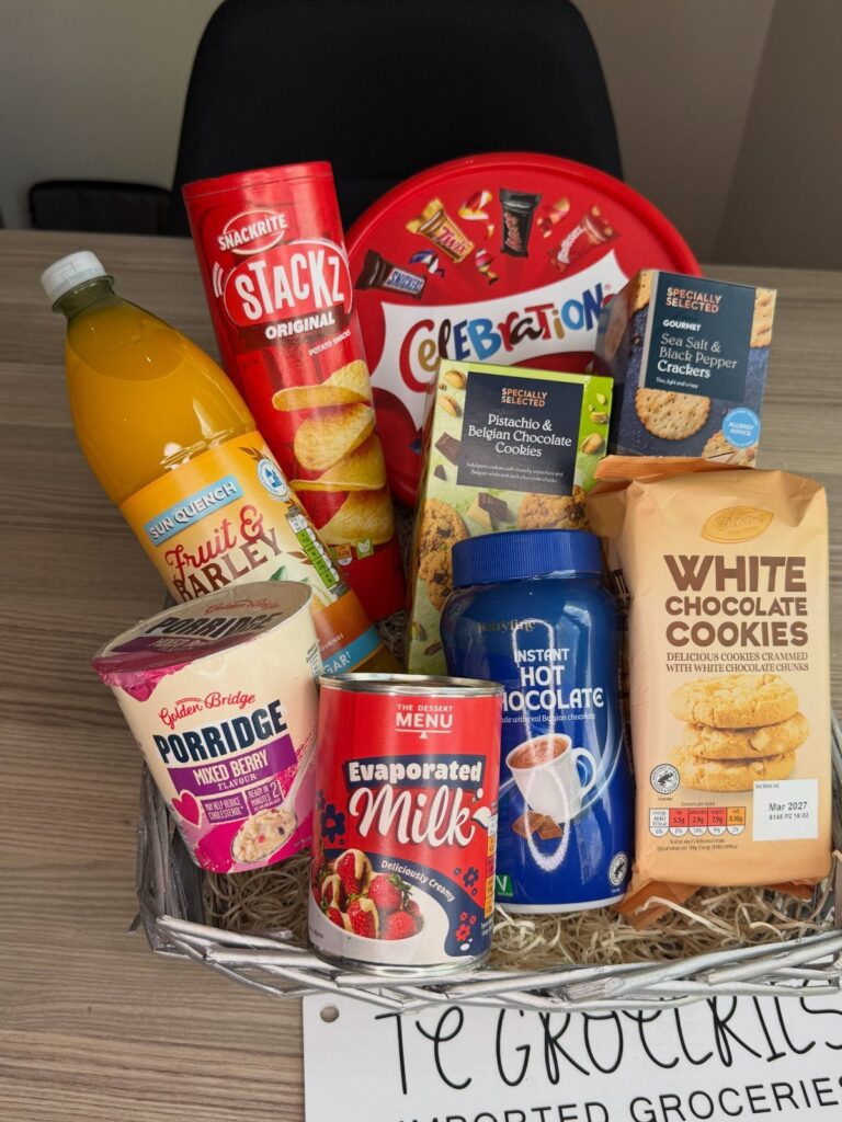 Grocery gift basket filled with snacks, juice, and pantry staples in a white basket.