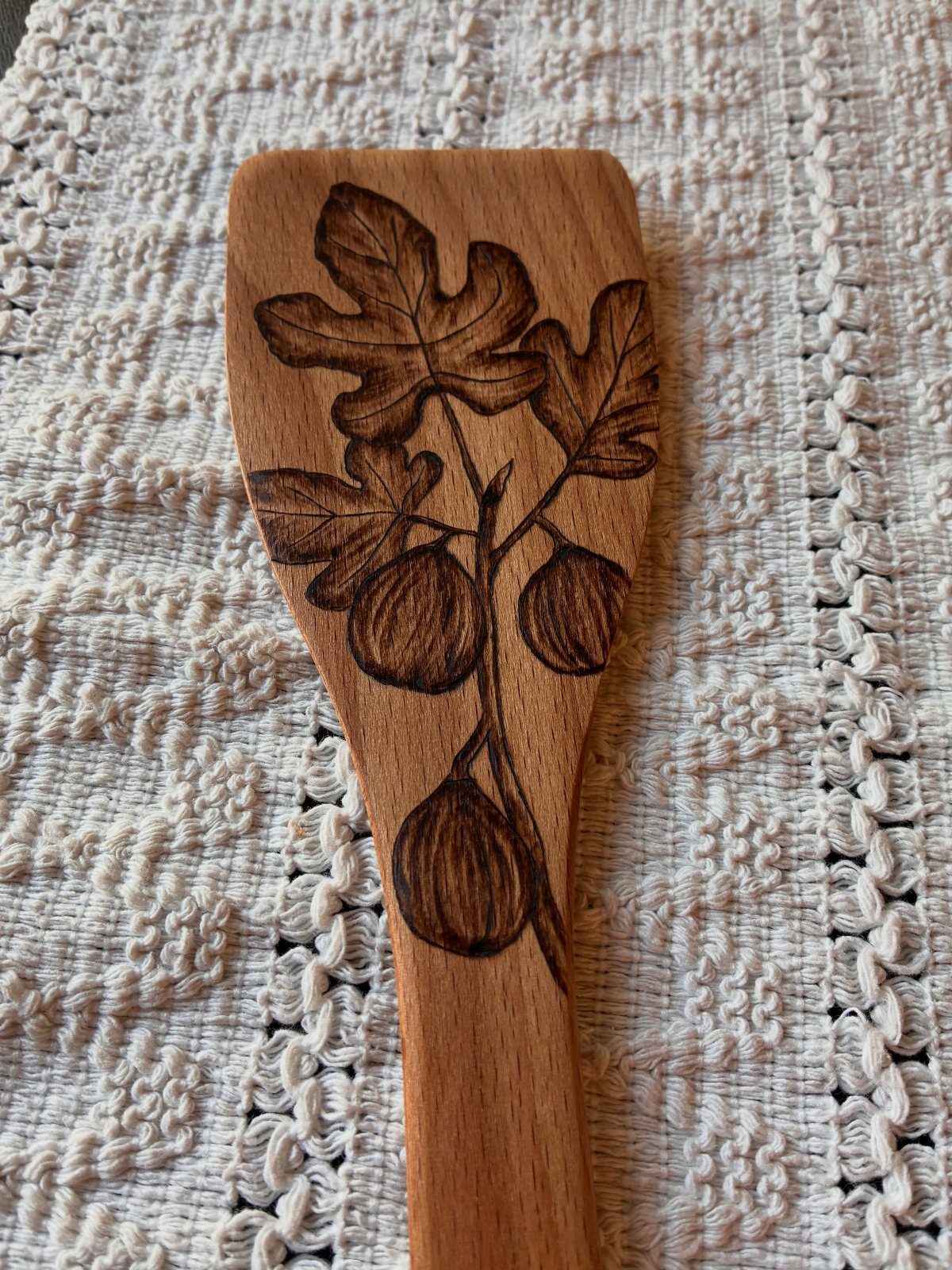 Wooden spoon with wood burned fig branch design on white lace background