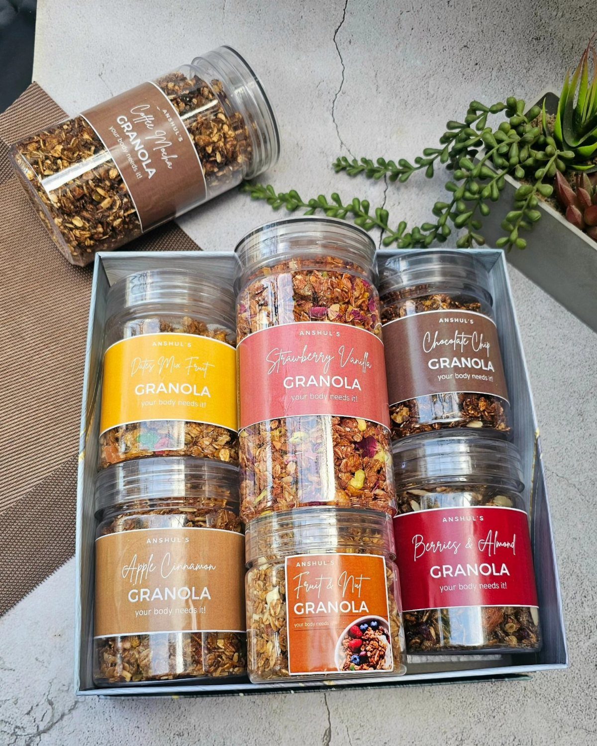 Glass jars filled with granola and colorful labels arranged in a gift box.