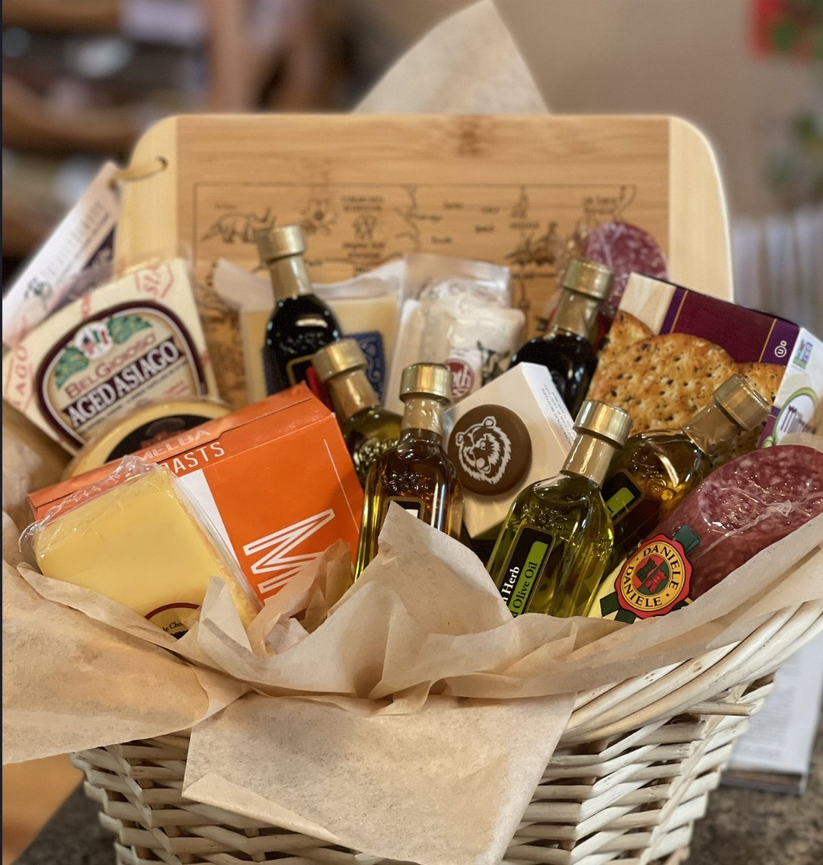 Gourmet gift basket with cheeses, olive oil, and cured meats in white wicker.