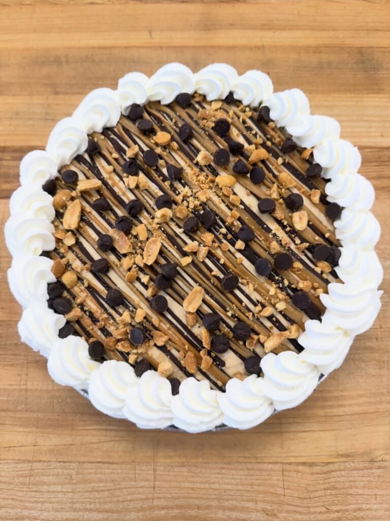 Round cake with chocolate drizzle, chocolate chips, and whipped cream on wooden table
