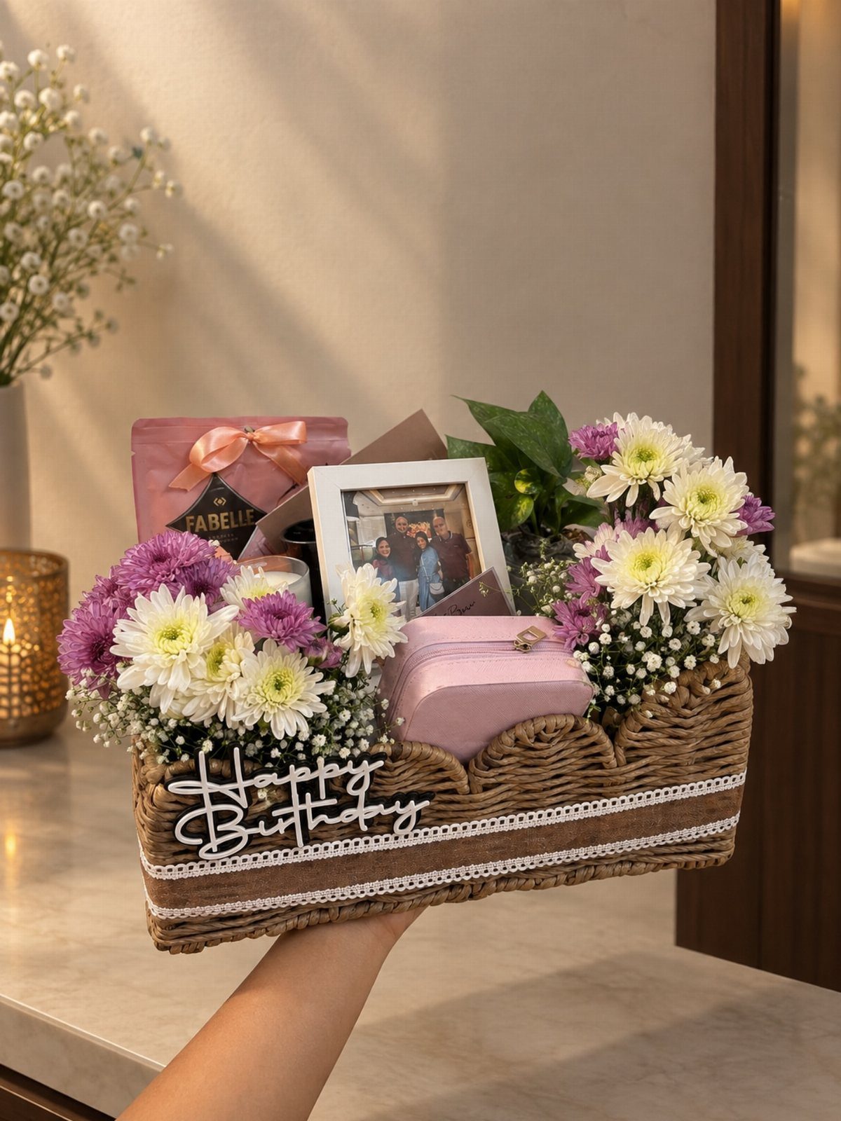 Wicker birthday gift basket with purple and white flowers, chocolates, and a photo frame.