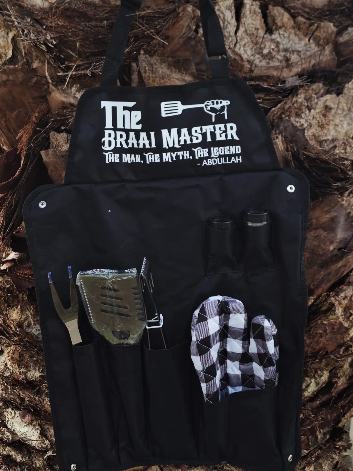 Black personalized apron for a braai master with cooking tools in the pockets.