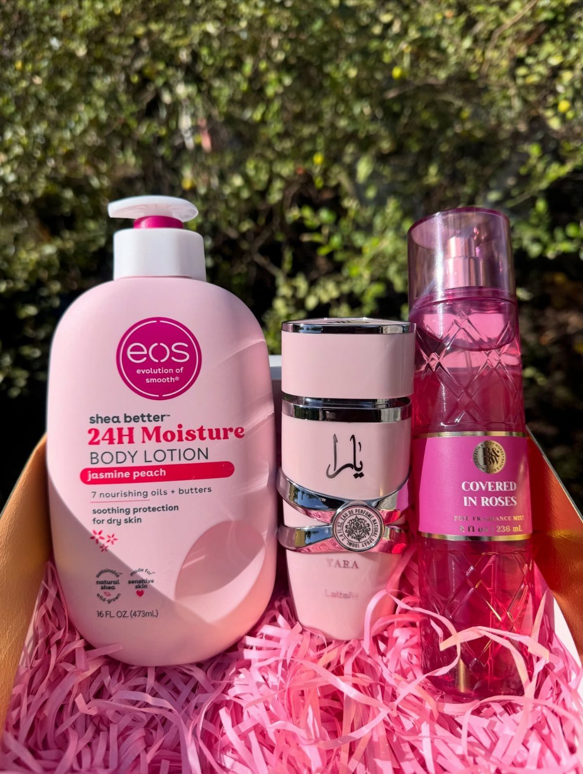 Pink body lotion, perfume, and fragrance spray in a pink shredded paper gift box.