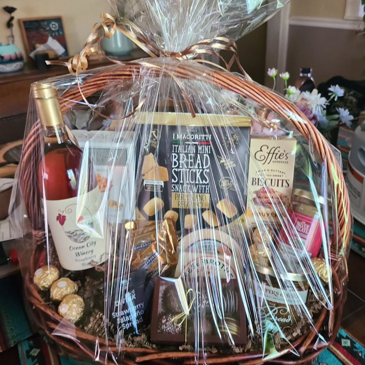 Wicker gift basket containing a bottle of rosé wine and various gourmet snacks.