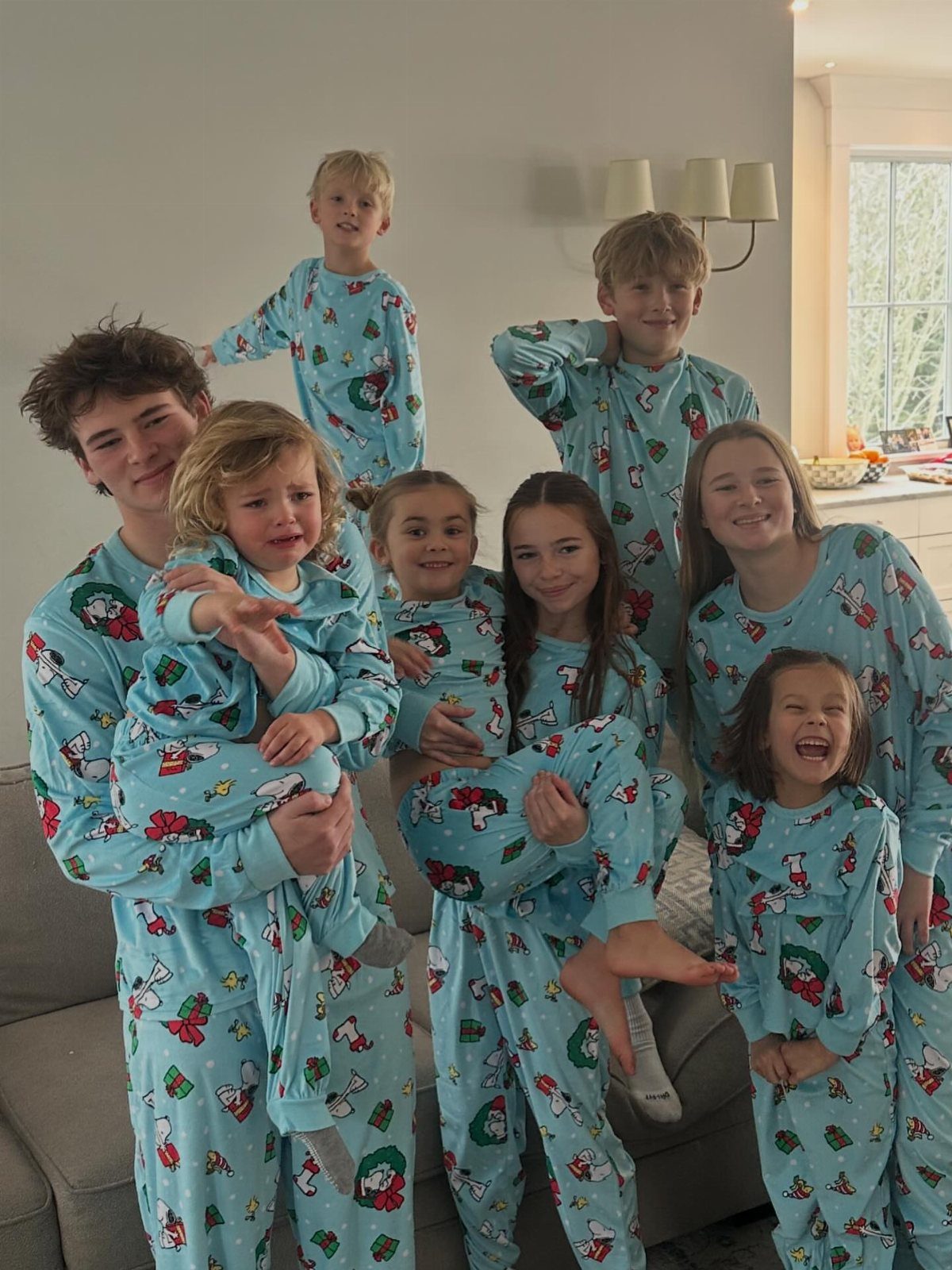 Family of eight wearing matching light blue holiday pajamas posing in a living room.