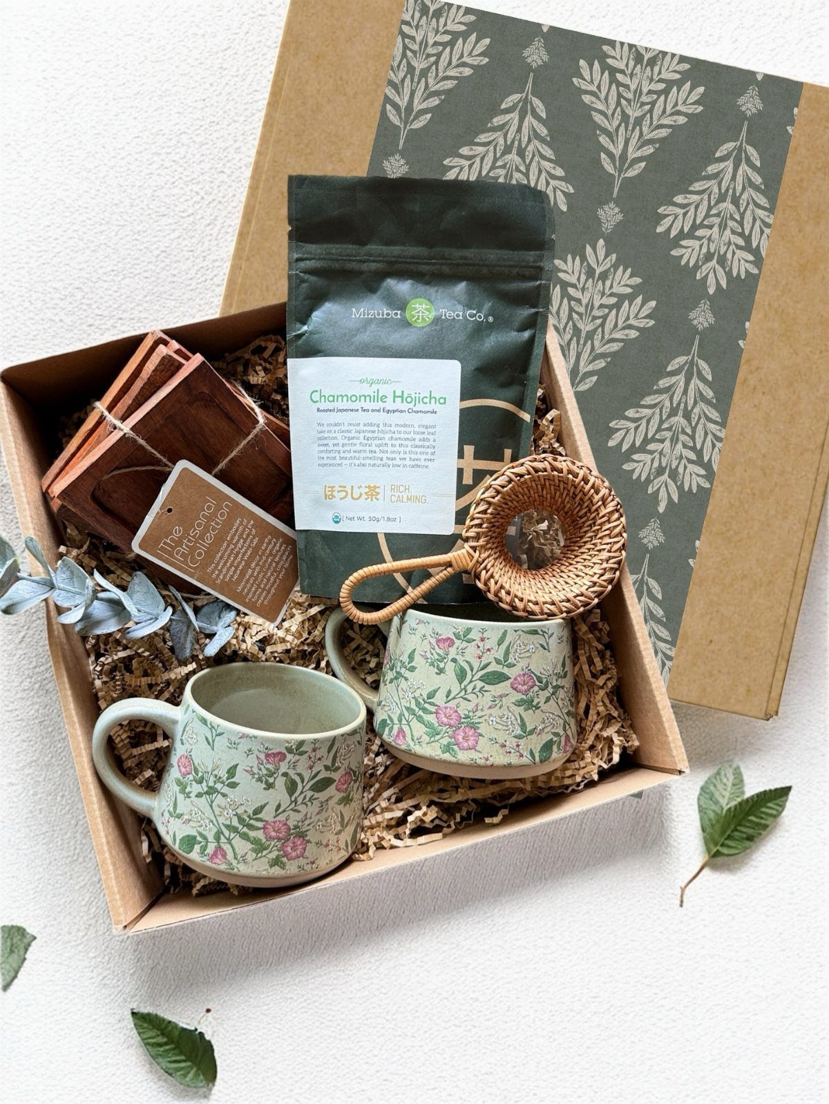 Tea gift set with floral mugs, tea pouch, and strainer in a cardboard box
