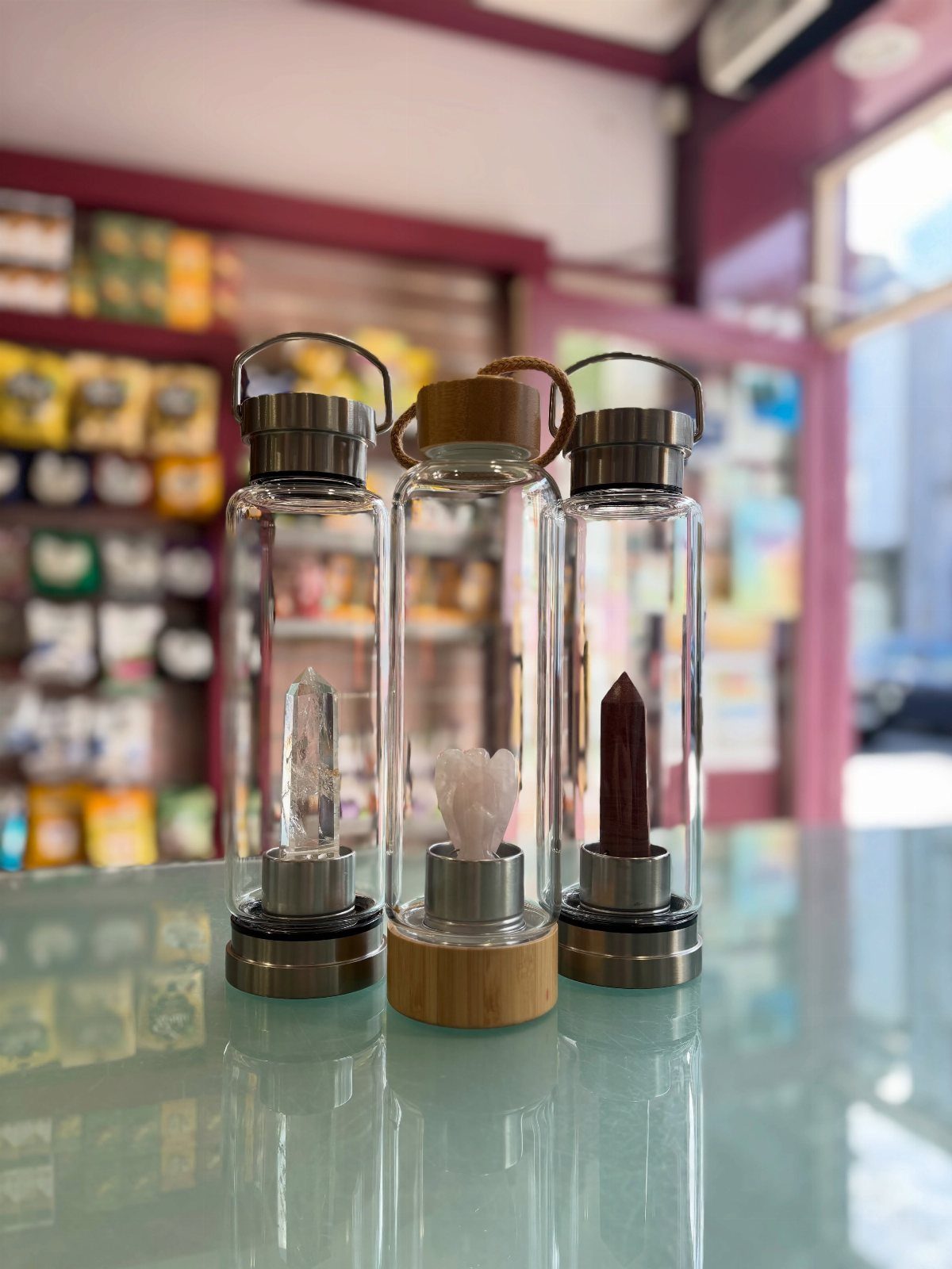Three glass water bottles containing different healing quartz crystals on a reflective surface.