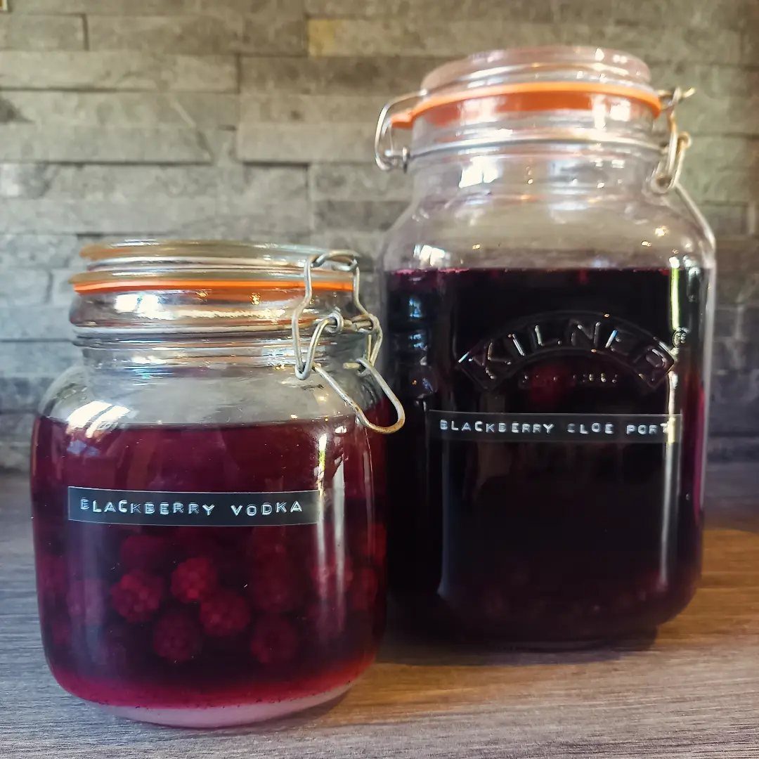 Two glass jars filled with homemade blackberry vodka and sloe port liqueurs.