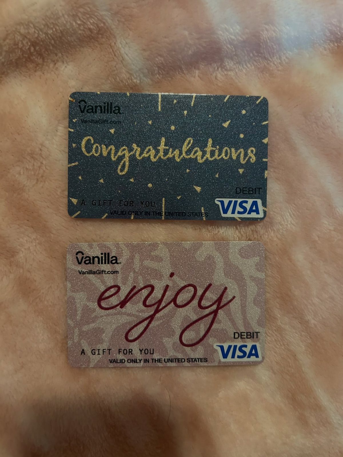 Two Vanilla Visa gift cards, one black and one silver, on peach fabric.
