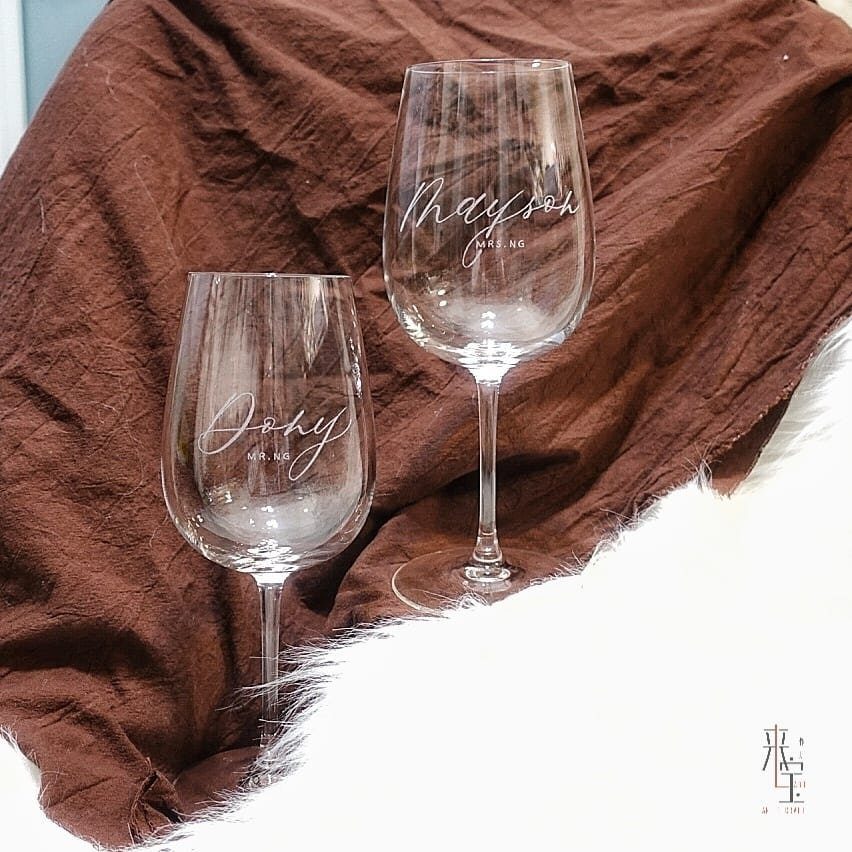 Two personalized wine glasses with etched names on a brown and white background.